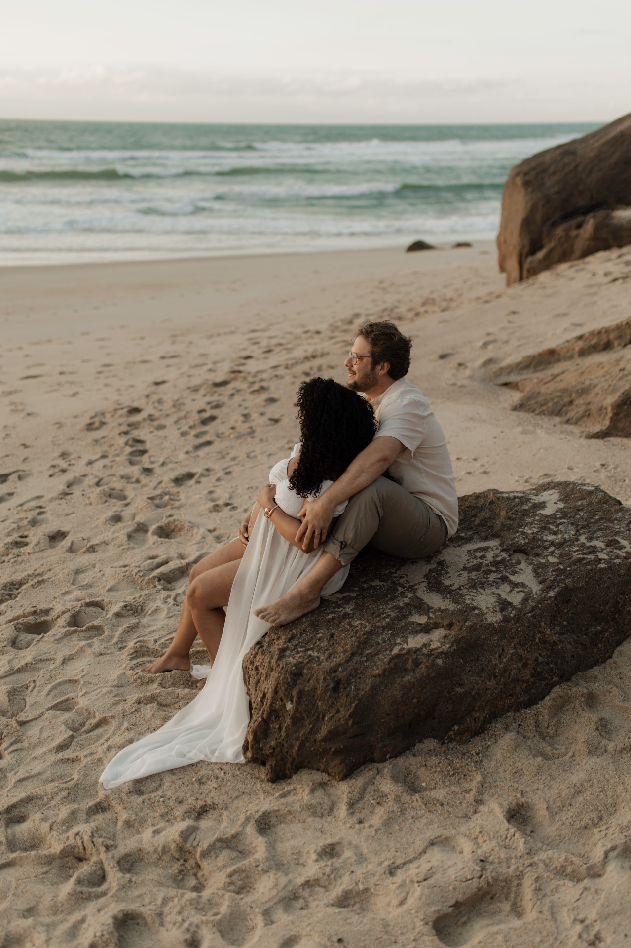 Casal grávido abraçado numa rocha à beira-mar