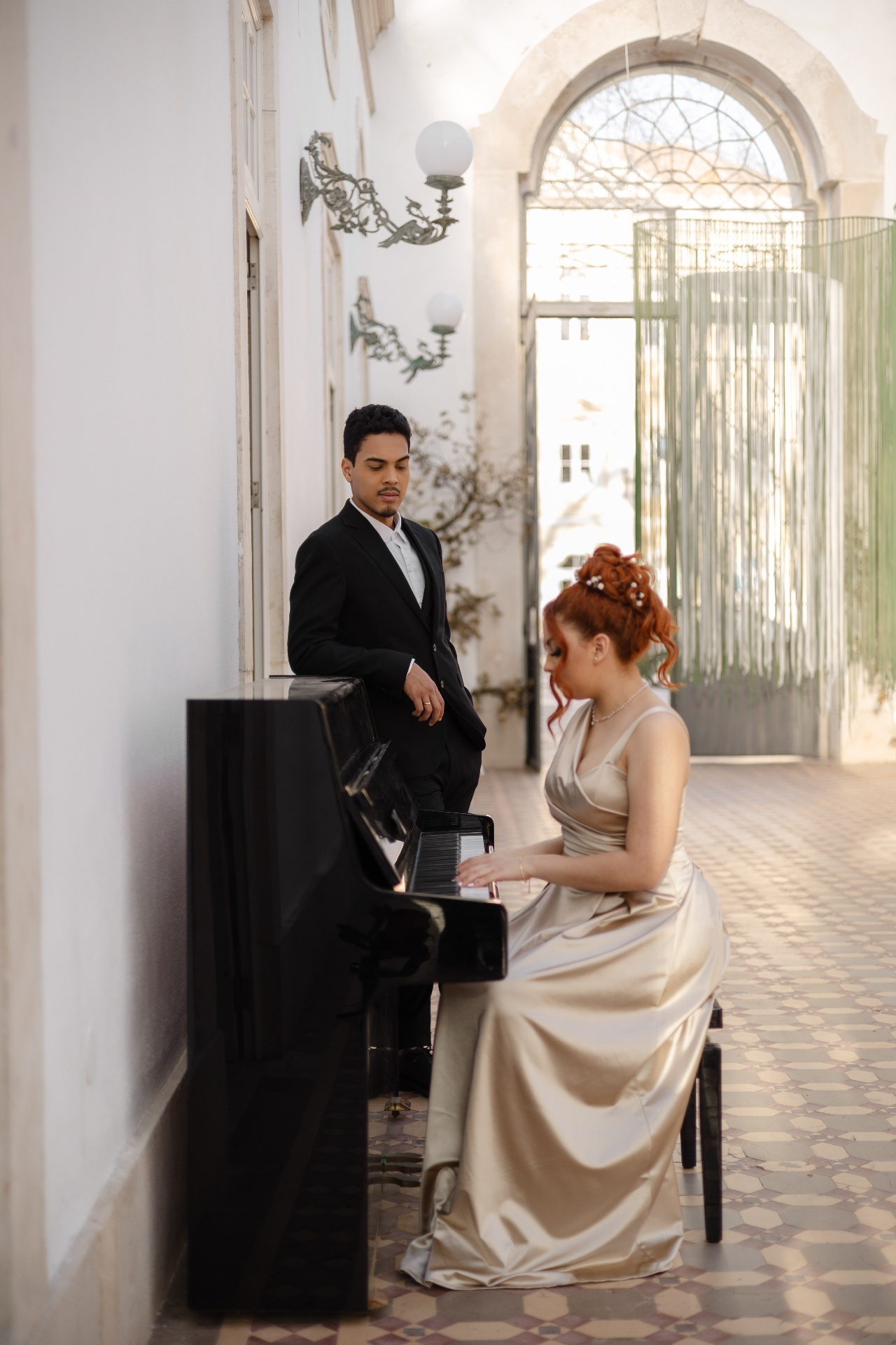Casal num palácio, ela ao piano e ele a observar